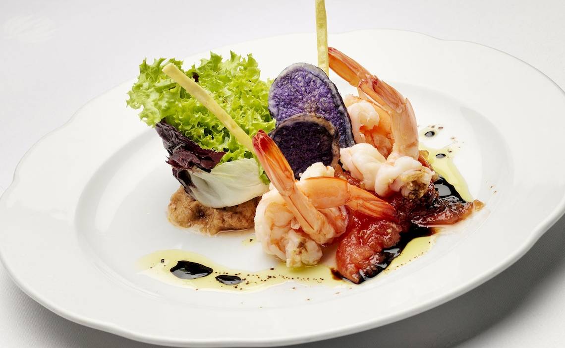 Elegantes Gericht mit Garnelen, Rotkohl und Beilagen auf einem weißen Teller.