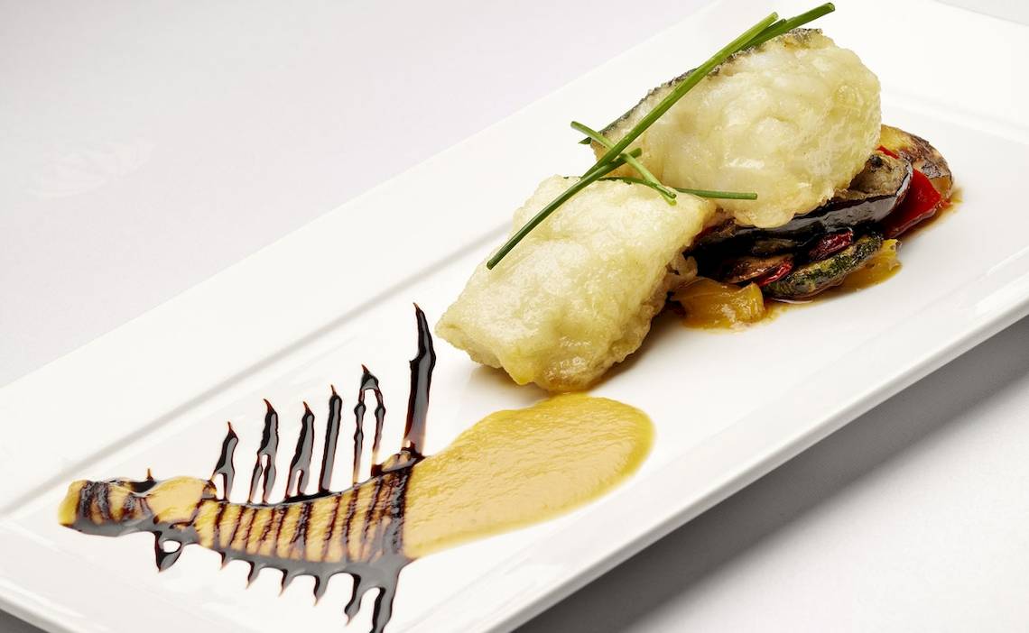 Gerecht auf weißem Teller mit Sauce und Gemüse, serviert mit Fisch.