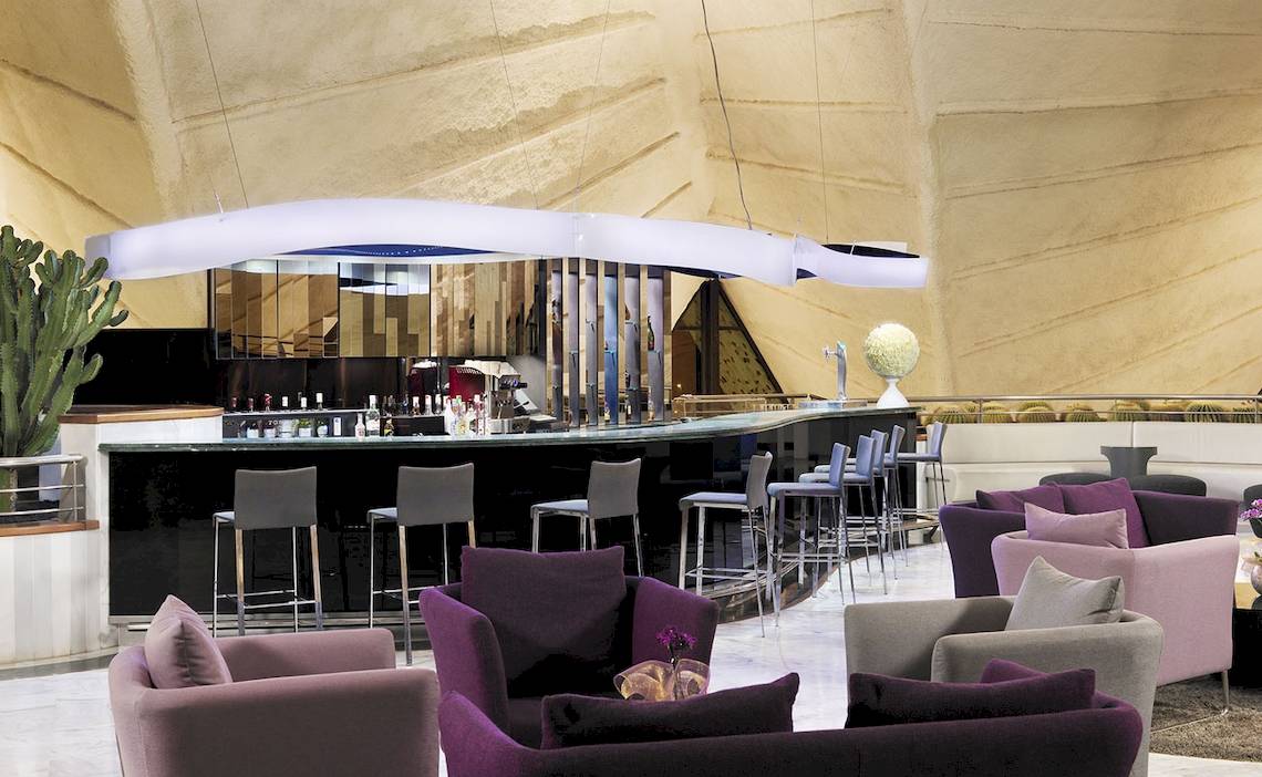 Loungebereich des H10 Playa Meloneras Palace mit einer Bar, Sitzgelegenheiten und Kakteen.