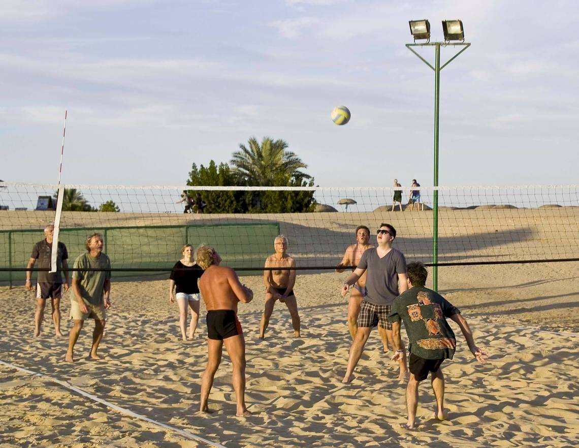 Gruppe von Spielern spielt Volleyball auf dem Sandstrand mit einem Netz.