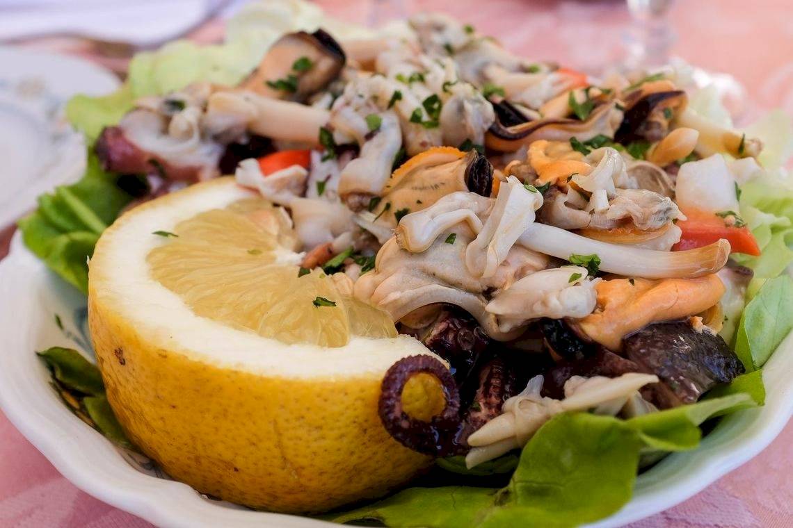 Salat mit Meeresfrüchten auf einem weißen Teller, inklusive Zitrone und Kräutern.
