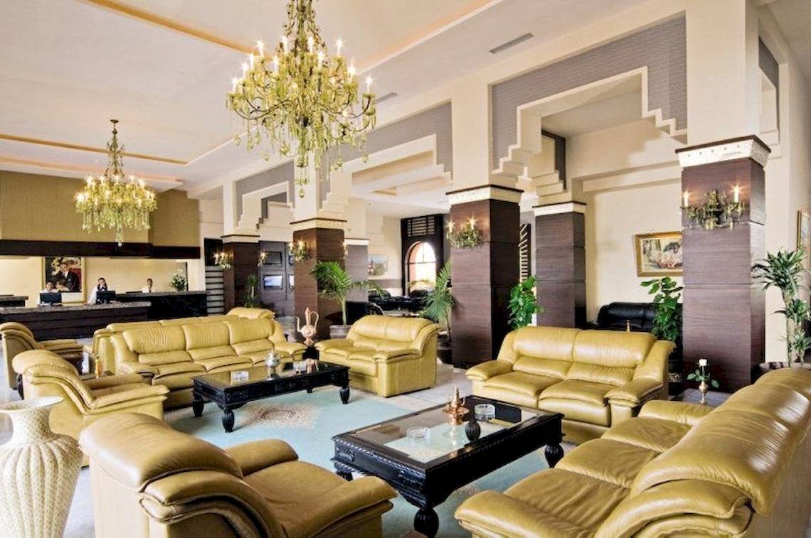 Lobby des Pickalbatros Aqua Fun Club Hotels mit goldenen Ledersofas, zwei Kronleuchtern und einem Empfangstresen.