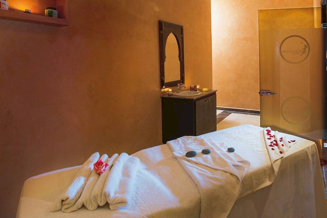 Massageraum im Hotel Pickalbatros Aqua Fun Club mit weißem Bett, Handtüchern, Rosenblättern und einem Spiegel.