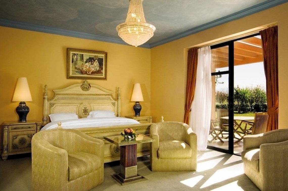 Luxuriöses Schlafzimmer im Pickalbatros Aqua Fun Club Hotel mit gelben Wänden, einem großen Bett, Kronleuchter und Möbeln.