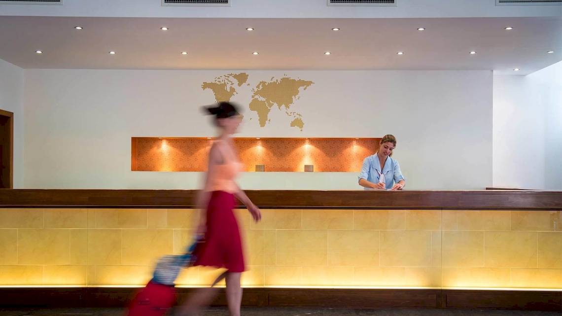 Eine Frau mit Koffern geht an der Rezeption des Bella Beach Hotels vorbei.
