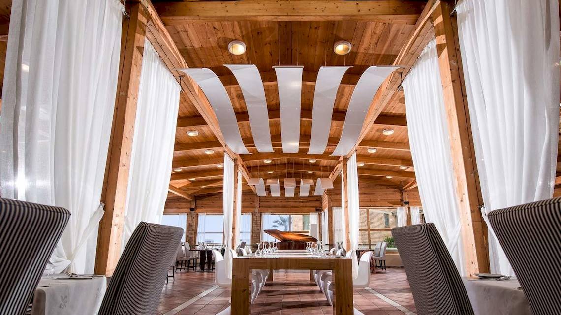 Innenbereich des Bella Beach Hotels mit Esstisch, Stühlen und weißen Vorhängen.