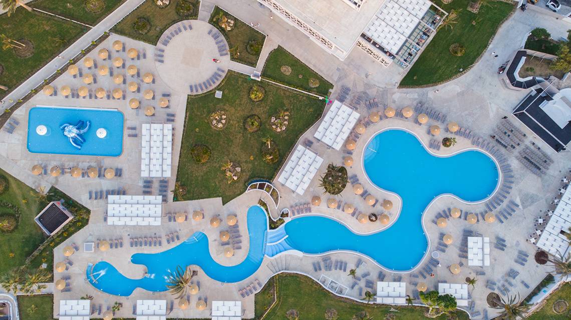 Luftaufnahme des Poolbereichs des Akti Imperial Deluxe Resorts mit zwei geschwungenen Pools, Sonnenliegen und Sonnenschirmen.