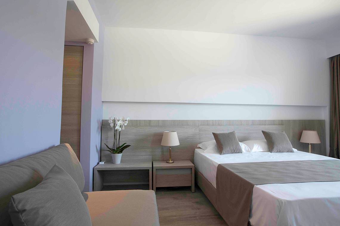Hotelschlafzimmer mit einem Bett, Sofa, zwei Nachttischen, Lampen und Blumen.