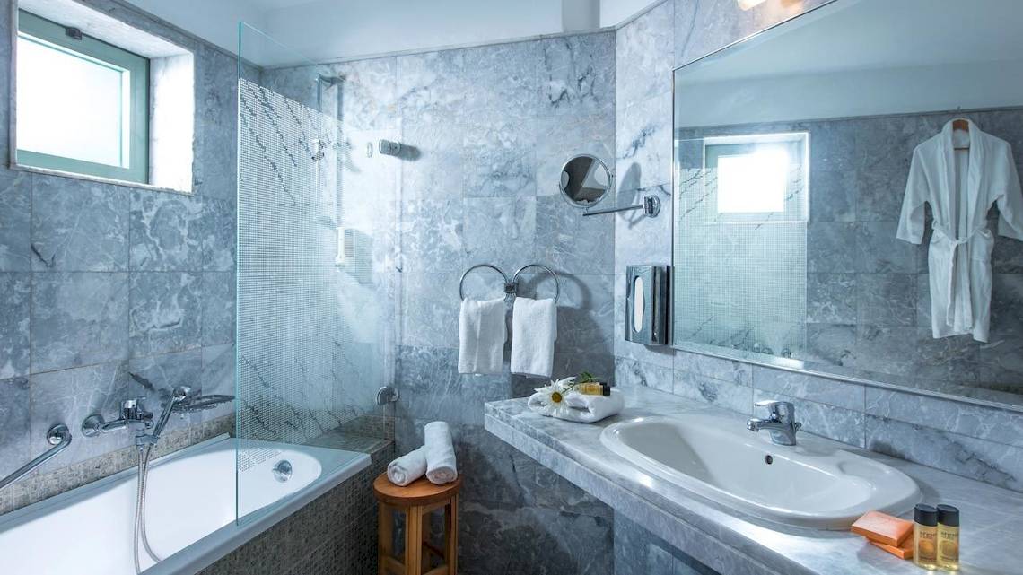Ein Badezimmer im Bella Beach Hotel mit Marmorwänden, einer Badewanne, einem Waschbecken und Handtüchern.