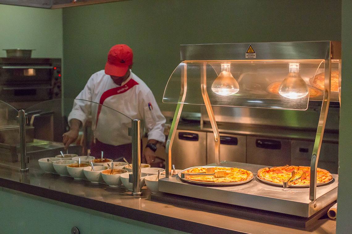 Koch im Restaurant des Akti Imperial Deluxe Resort & Spa, der eine Pizza unter einem Heizlicht serviert