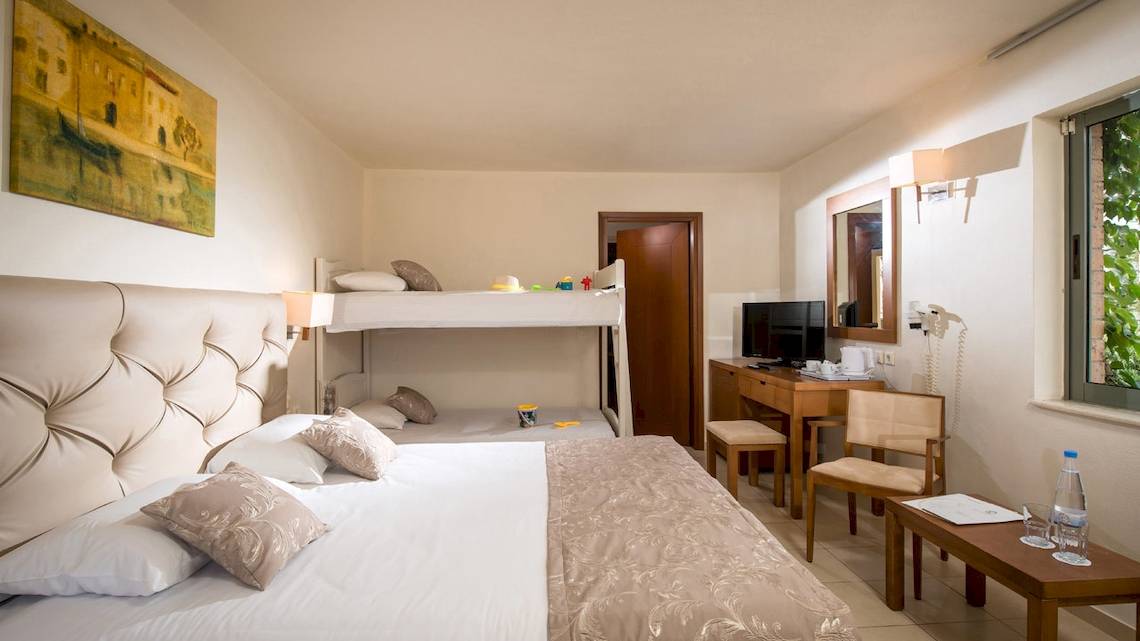 Doppelzimmer im Bella Beach Hotel mit Doppelbett und Stockbett, Nachttisch und Schreibtisch.