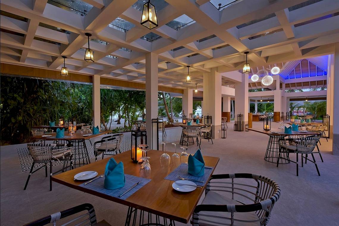 Innenansicht des Restaurants des Kandima Maldives Hotels mit gedeckten Tischen und hängenden Lampen.