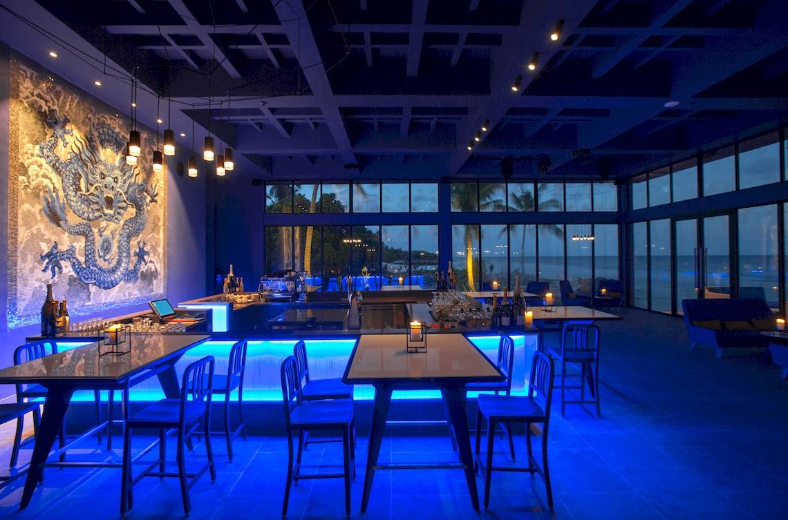 Innenansicht der Bar im Kandima Maldives Hotel mit blauer Beleuchtung und Meerblick.