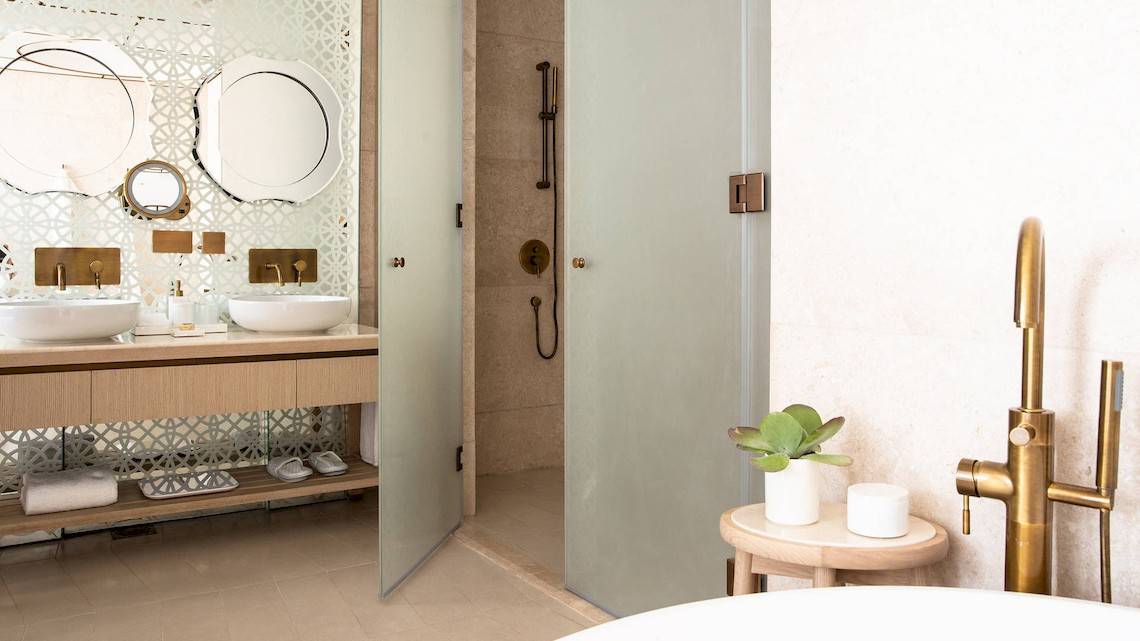 Badezimmer im Jumeirah at Saadiyat Island Resort mit zwei Waschbecken, Regendusche und goldenen Armaturen.