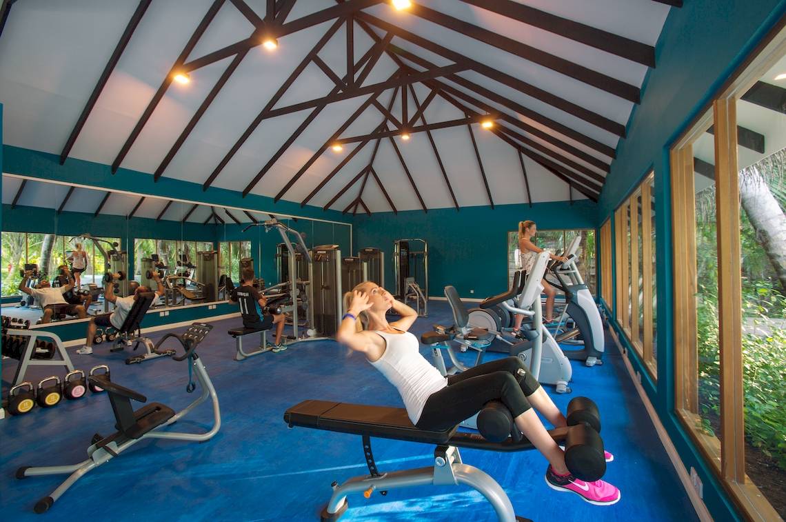 Fitnessstudio im Kandima Maldives Hotel mit Personen, die Hanteln benutzen und eine Frau auf einer Bank trainiert.