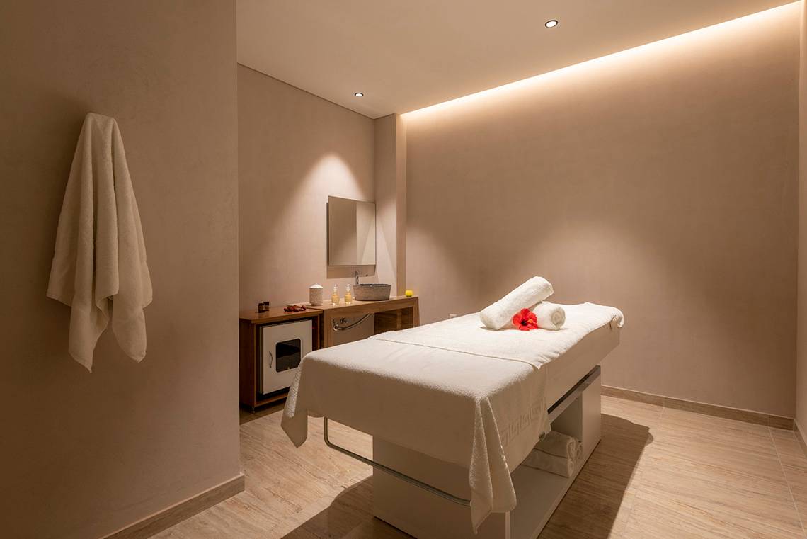 Spa-Behandlungsraum im Horizon Beach Resort mit weißer Liege, roten Blumen, und beleuchteten Wänden.