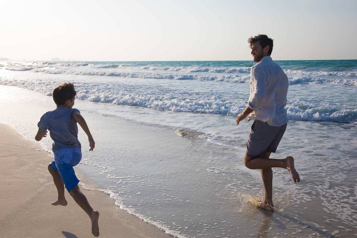Vater und Sohn laufen am Strand im Jumeirah at Saadiyat Island Resort