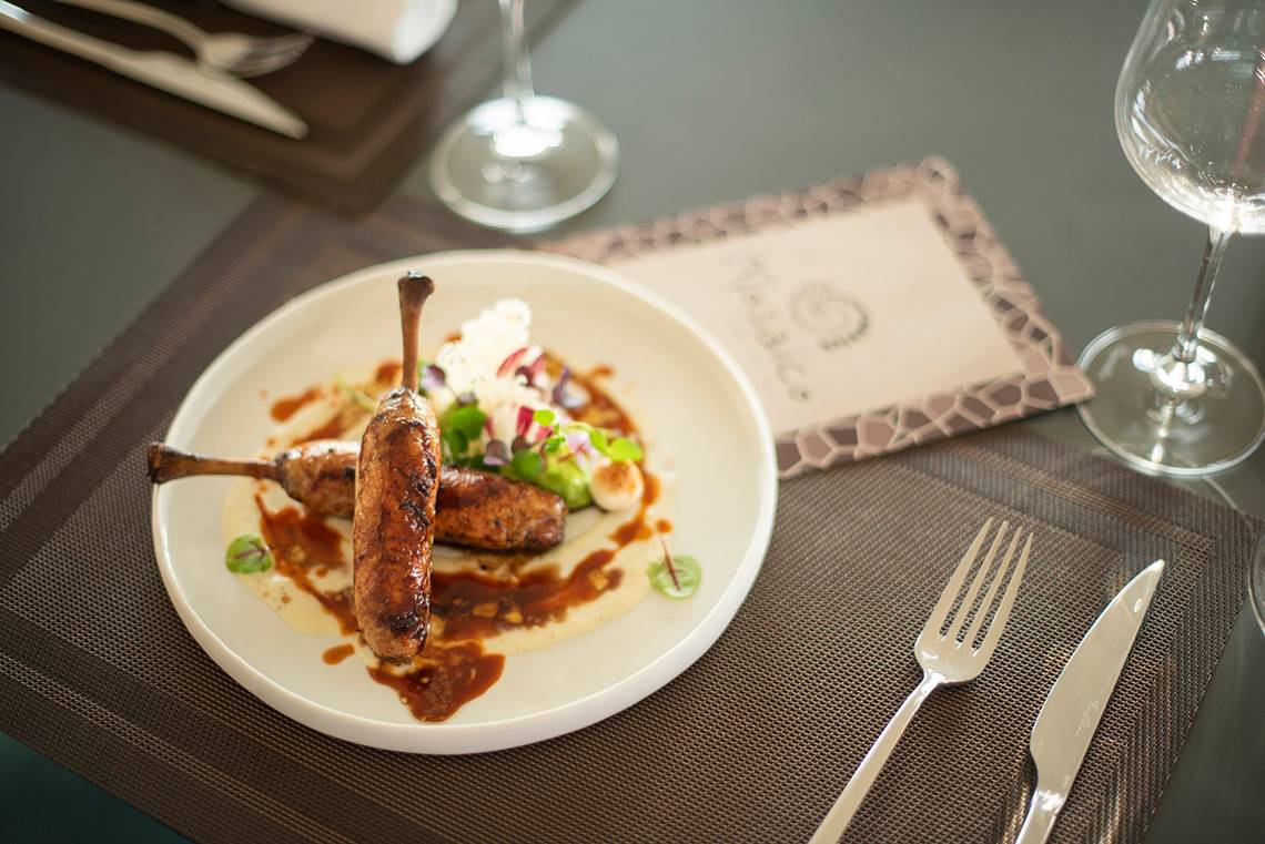 Gebratene Wurst auf einem weißen Teller mit Sauce und Gemüse.