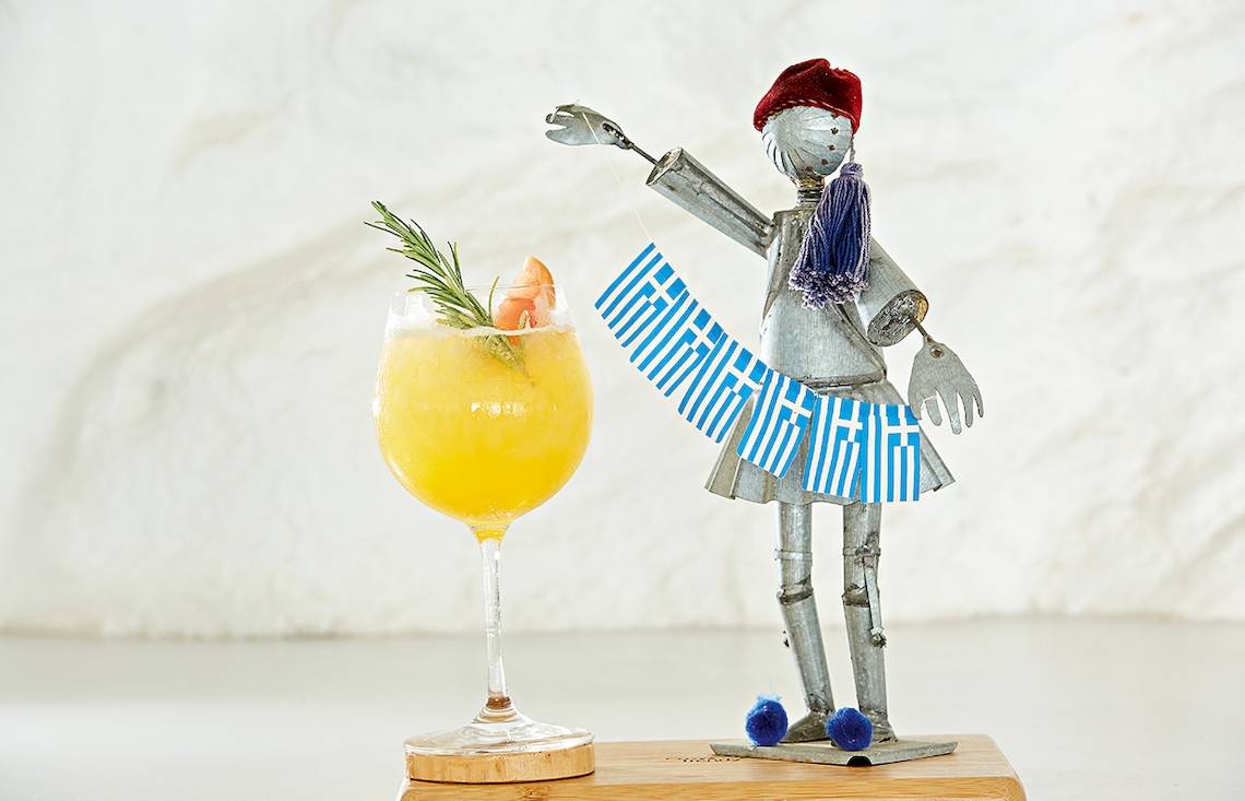Ein Cocktailglas mit einem griechischen Dekofigure, die eine Flagge hält.