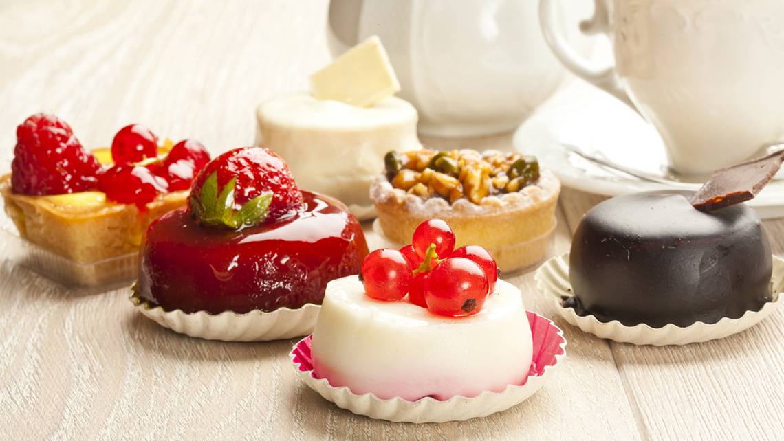 Verschiedene Desserts auf einem Holztisch, darunter eine Tarte mit Himbeeren und eine Schokoladentarte.