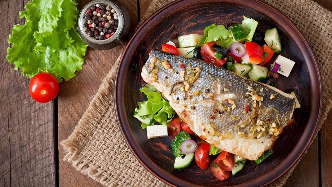 Ein Teller mit gegrilltem Lachs und gemischtem Salat auf einem Holztisch.