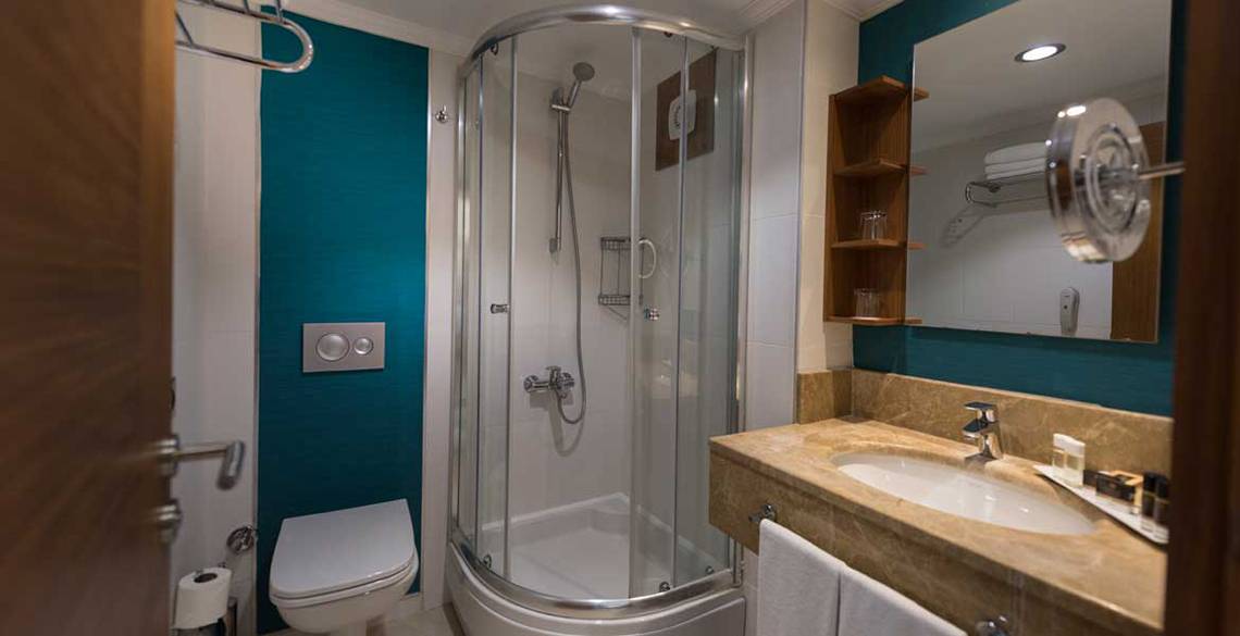 Badezimmer im Kamelya Aishen K Club Hotel mit Glasdusche, Waschbecken und Spiegel.