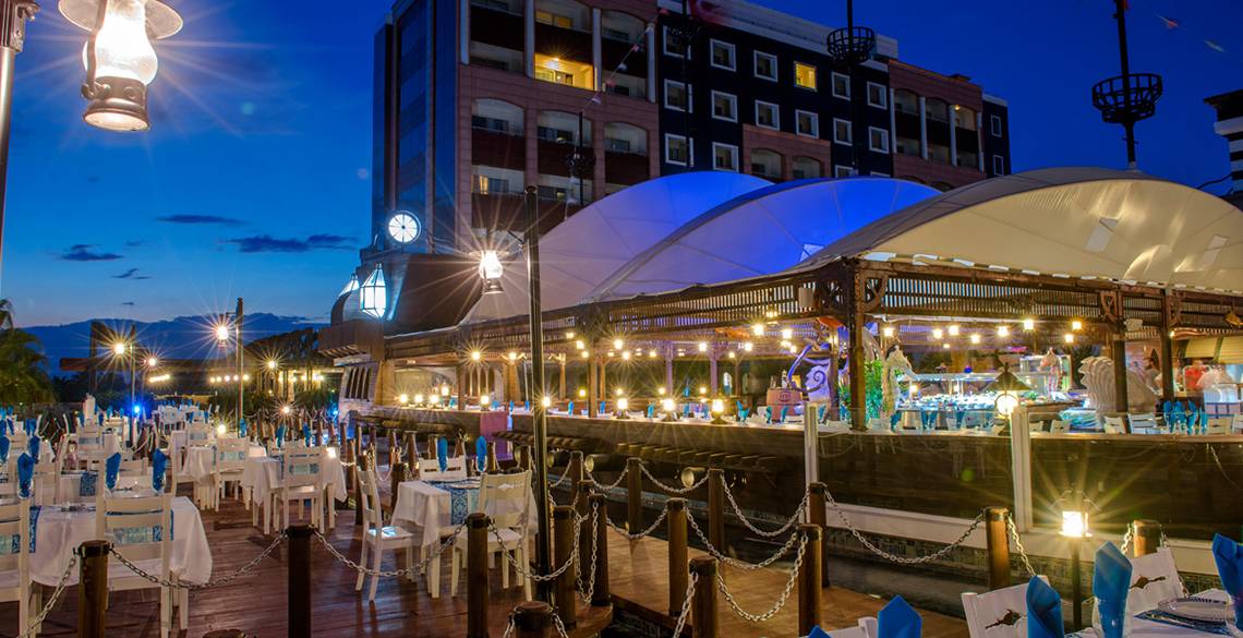 Dinnerbereich des Kamelya Aishen K Club Hotels bei Nacht, mit vielen gedeckten Tischen und leuchtenden Lichtern.