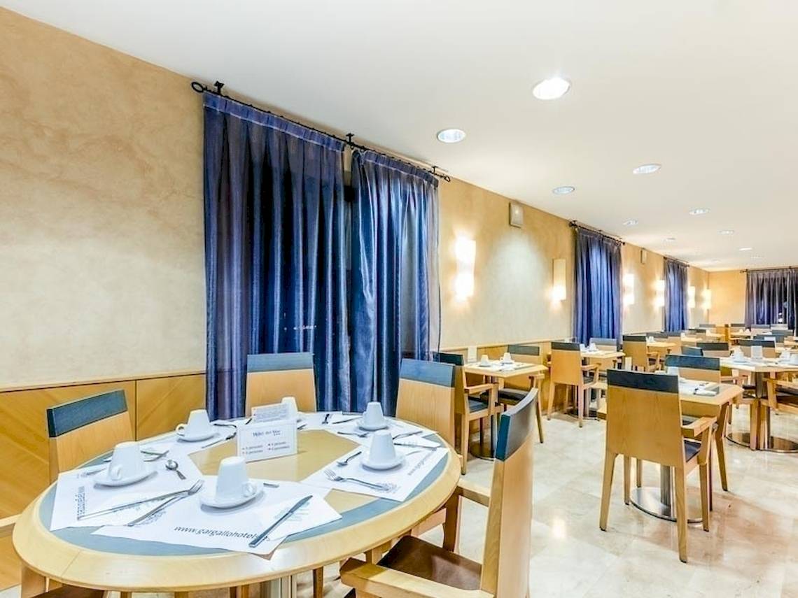 Frühstücksraum des Del Mar - Barcelona Hotels mit blauen Vorhängen und runden Tischen.