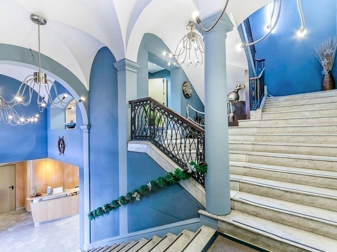 Der Eingangsbereich des Del Mar - Barcelona Hotels mit blauen Wänden, weißen Marmortreppen und schmiedeeisernem Geländer.