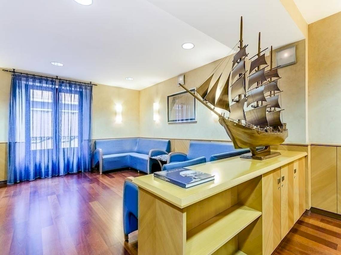 Innenraum des Del Mar - Barcelona Hotels mit blauen Sofas und einem Modellschiff auf einem Holztisch.