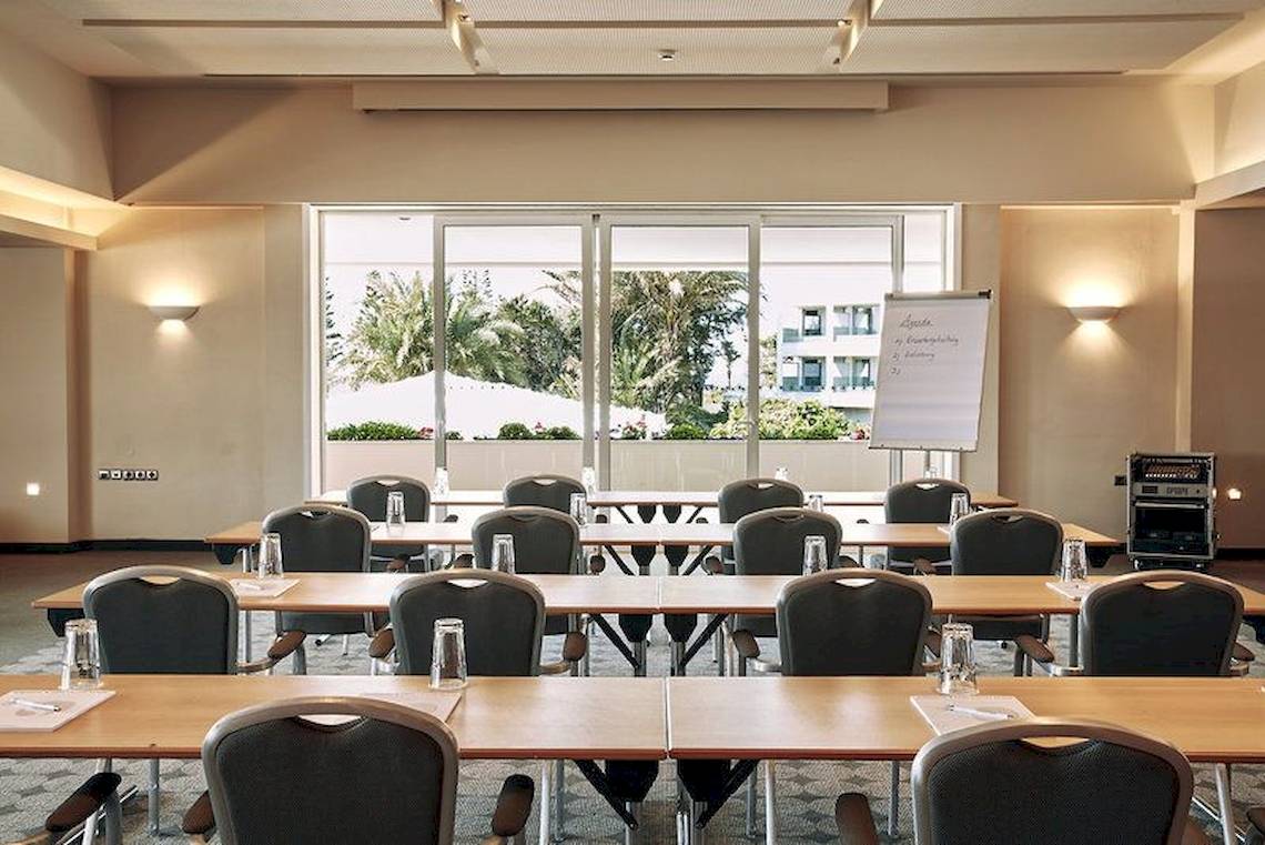 Konferenzraum im Robinson Kyllini Beach Hotel mit Blick auf eine weiße Tafel und Palmen draußen.