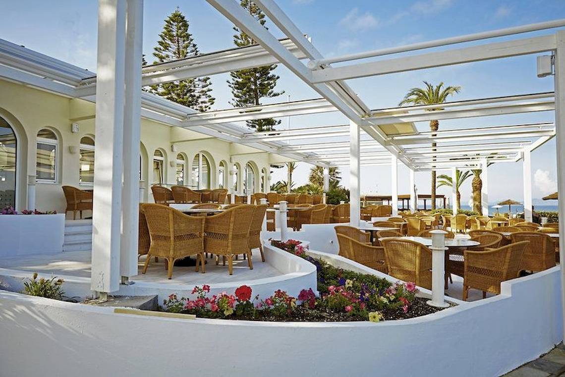 Außenterrasse des Robinson Kyllini Beach Hotels mit Tischen und Stühlen unter einem Pergoladach.