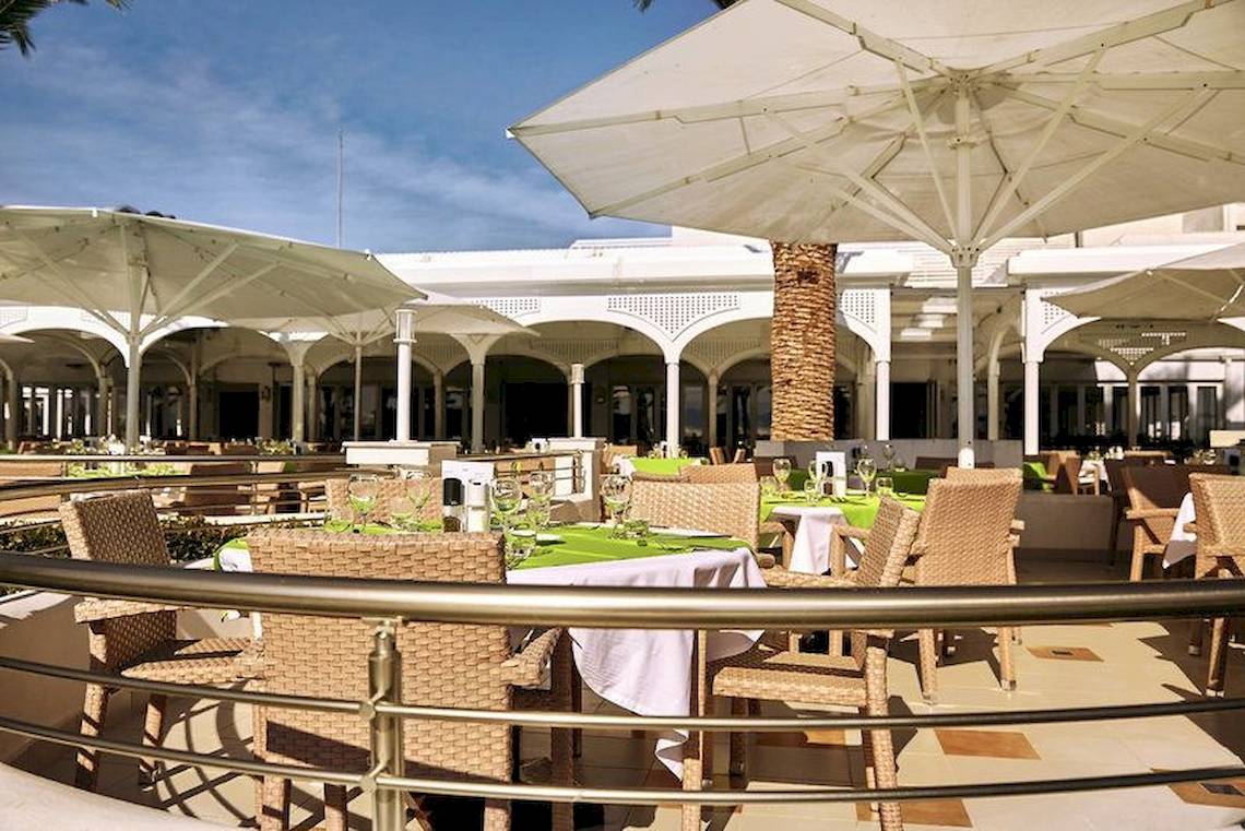 Außenterrasse des Robinson Kyllini Beach Hotels mit Tischen und Stühlen unter Schirmen.