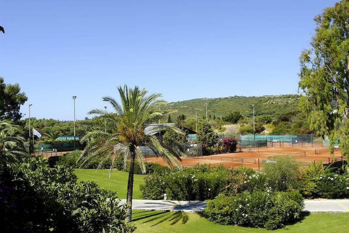 Tennisplatz im Freien im Robinson Kyllini Beach Hotel mit grünem Rasen und Palmen.