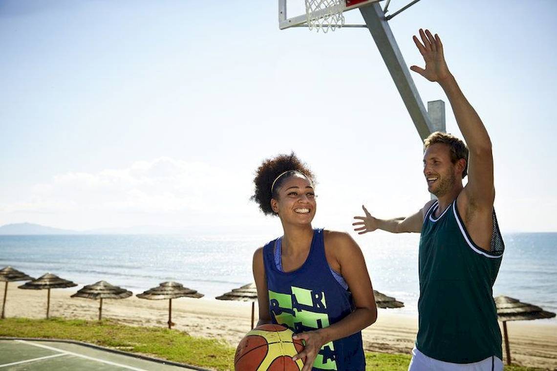 Ein Paar spielt Basketball am Strand mit einer Frau, die den Ball hält, und einem Mann, der nach dem Ball greift.