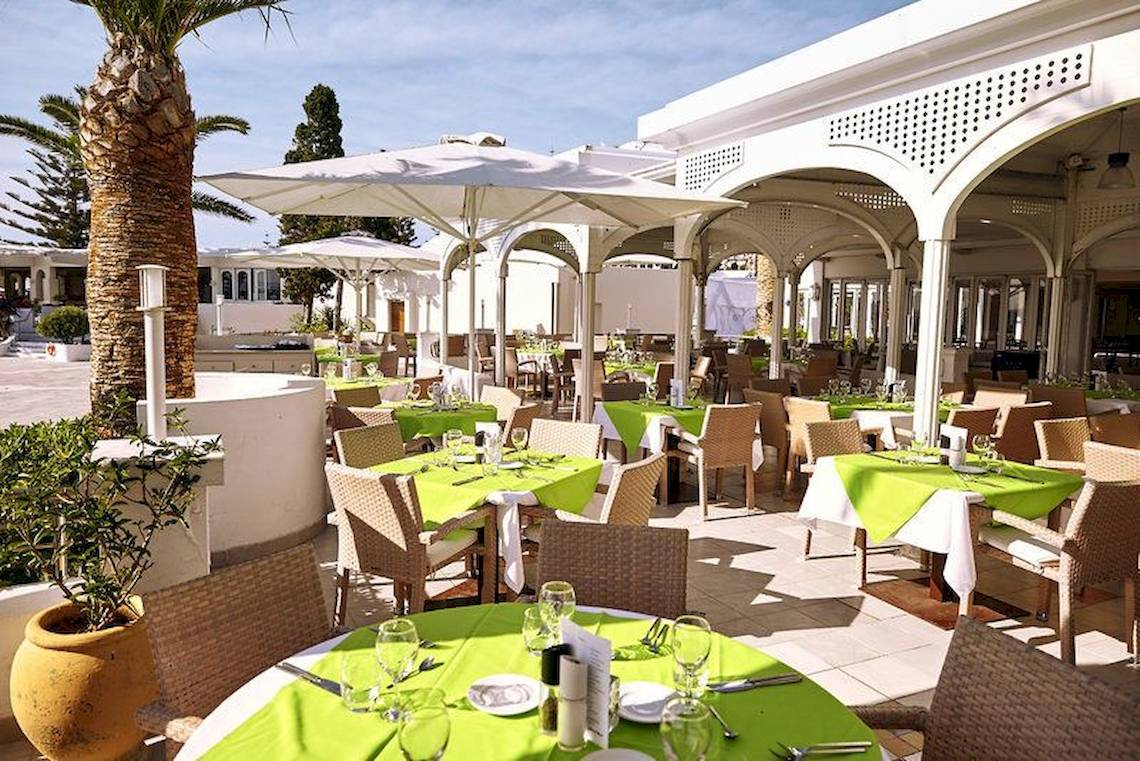 Außenbereich des Robinson Kyllini Beach Hotels mit gedeckten Tischen und weißen Sonnenschirmen.