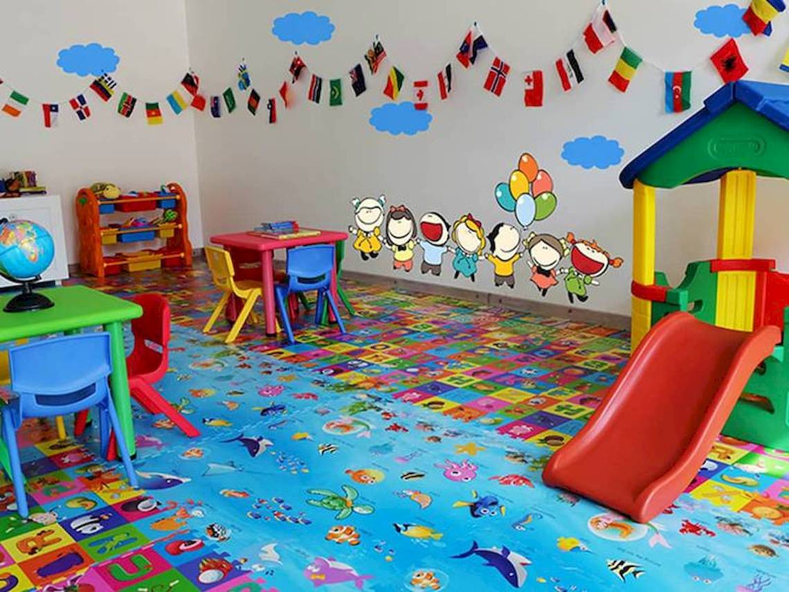 Kinderzimmer im Amaya Kuda Rah Hotel mit bunten Teppich, Tischen, Stühlen und Wandaufkleber.