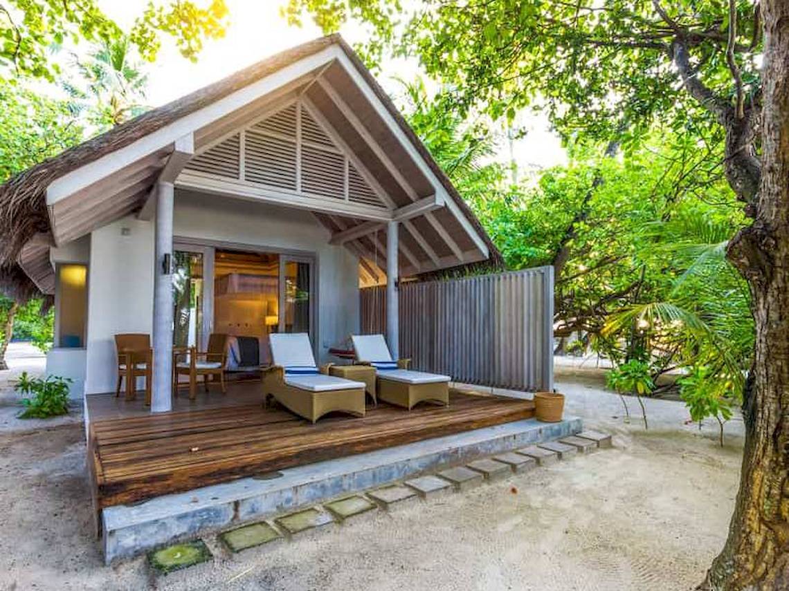 Foto eines Ferienhauses im Freien mit Sonnenliegen, Stühlen und einem Tisch auf einer Holzterrasse, umgeben von Bäumen.