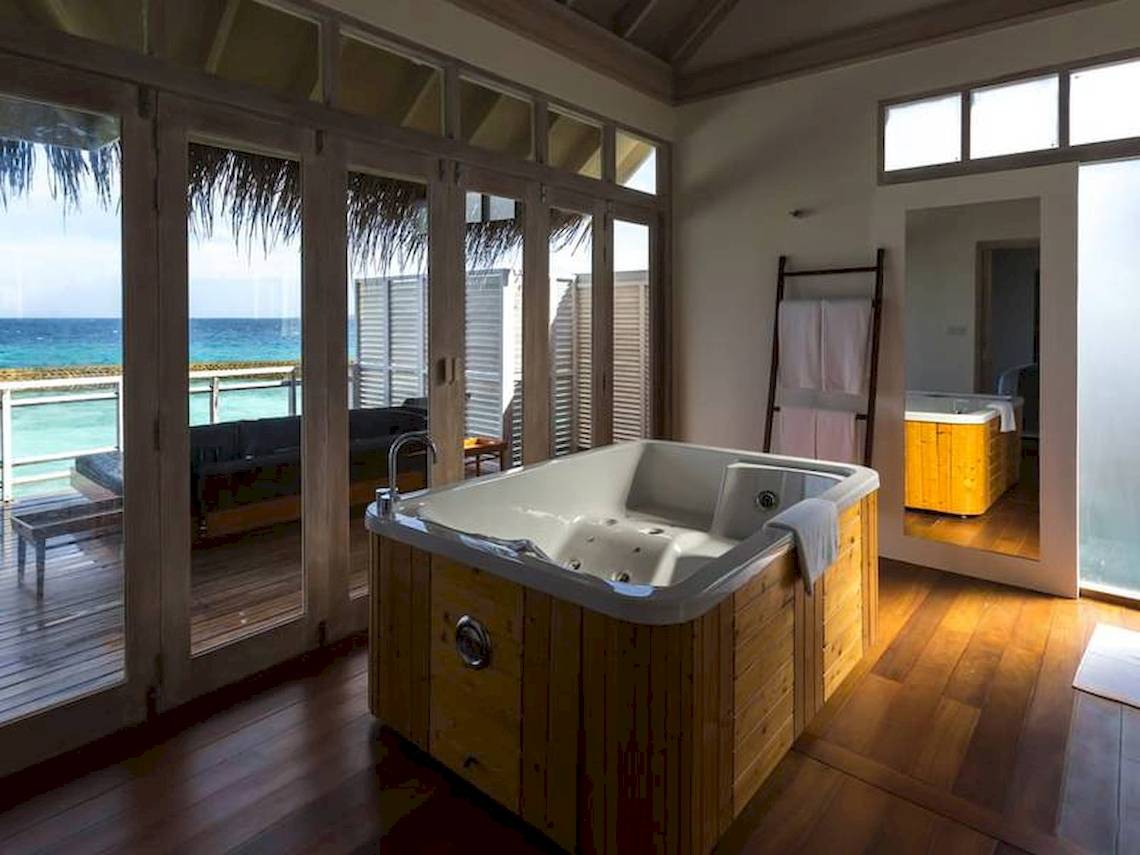 Ein Badezimmer mit einem Whirlpool im Freien, der an einen Balkon angrenzt, mit Blick auf das Meer und ein Sofa.