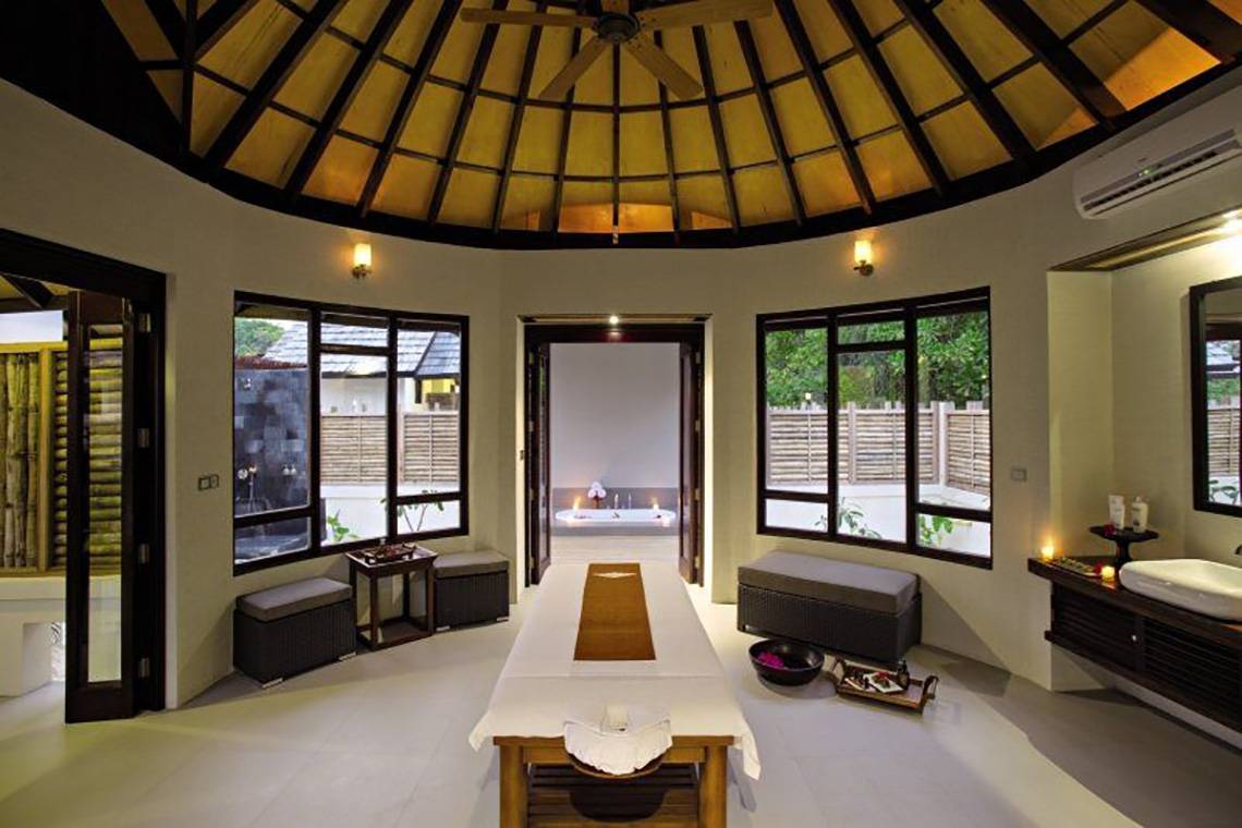 Massagebereich im Atmosphere Kanifushi Maldives mit Behandlungstisch, Badewanne und Fenstern.