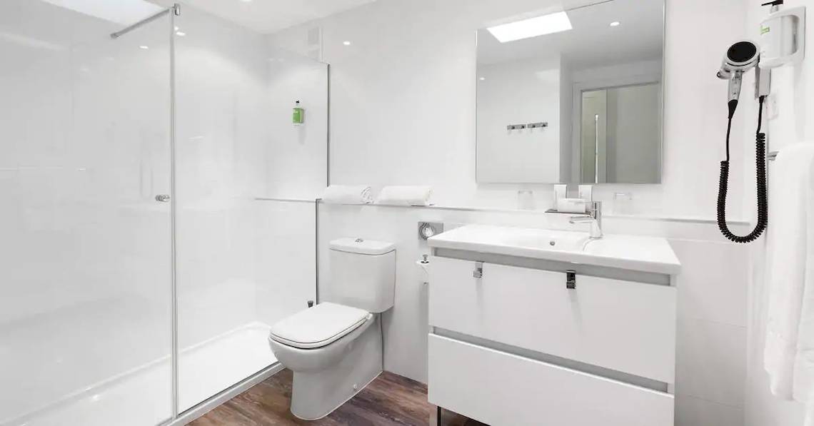 Ein modernes Badezimmer mit weißer Dusche, Toilette, Waschbecken und Spiegel im Sol Fuerteventura Jandia Hotel.