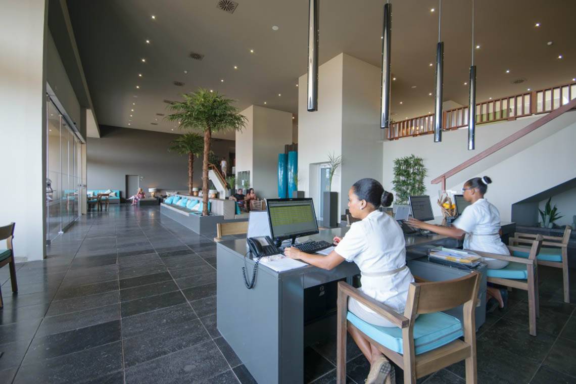 Rezeption im Oasis Salinas Sea Hotel mit zwei Angestellten und Gästen im Hintergrund.