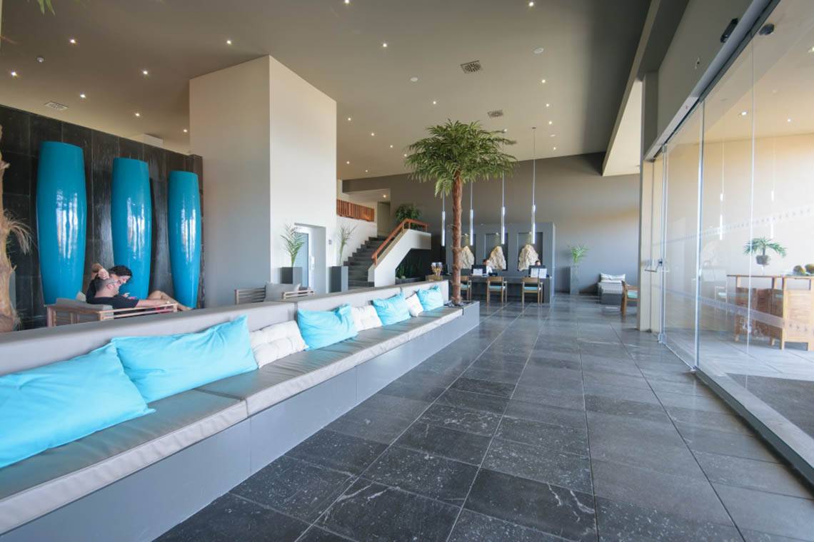 Lobby des Oasis Salinas Sea Hotels mit langen grauen Sofas, blauen Kissen und großen blauen Säulen.