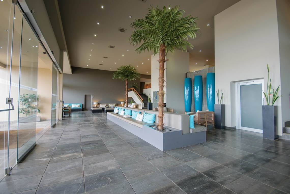 Lobby des Oasis Salinas Sea Hotels mit gepolsterten Bänken, Palmen und blauen Vasen.