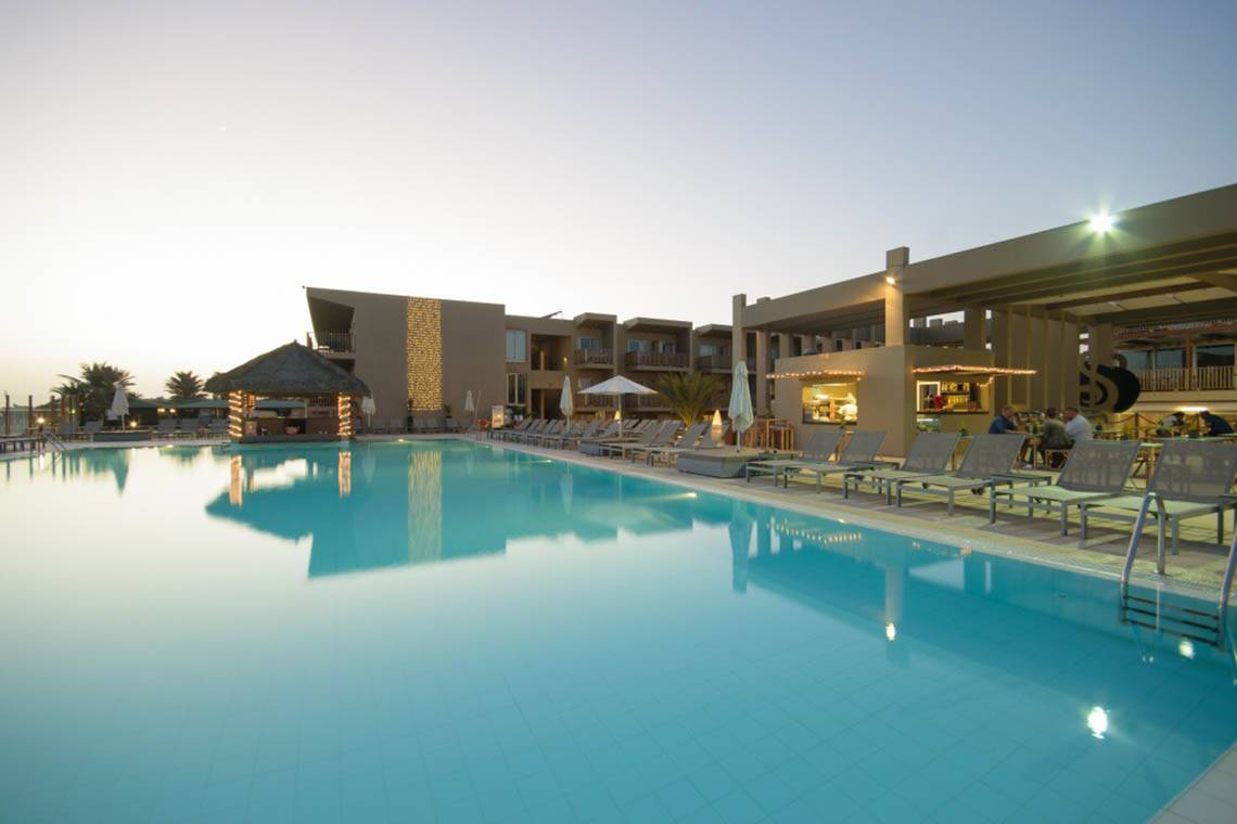 Außenbereich des Oasis Salinas Sea Hotel mit Swimmingpool und Sonnenliegen bei Sonnenuntergang.