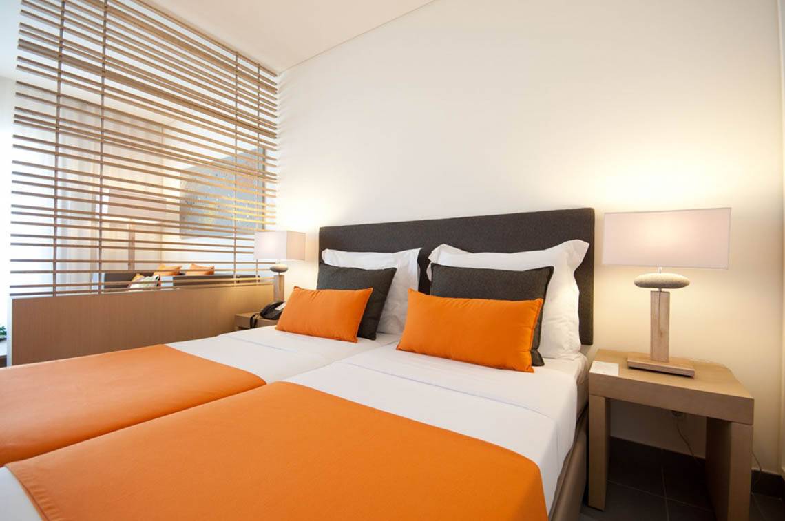 Doppelbett im Hotelzimmer Oasis Salinas Sea mit orangefarbenen Kissen und weißen Decken.