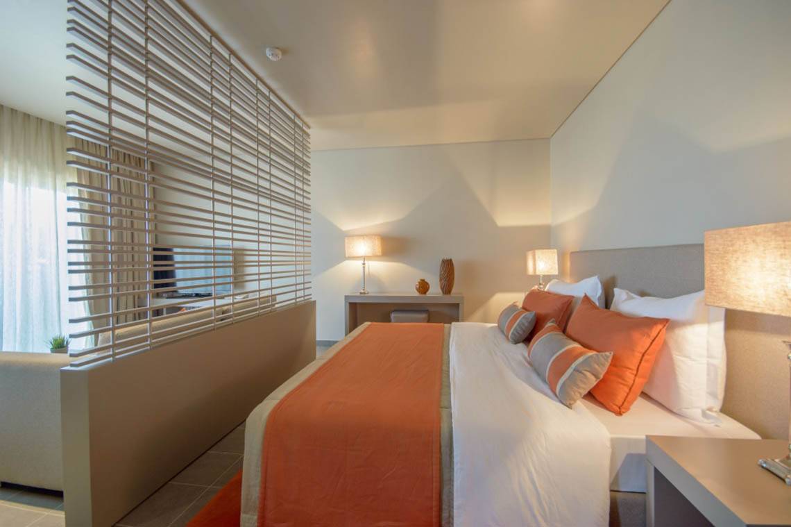 Schlafzimmer im Oasis Salinas Sea Hotel mit einem großen Bett, weißen und orangefarbenen Kissen und Nachttischen mit Lampen.