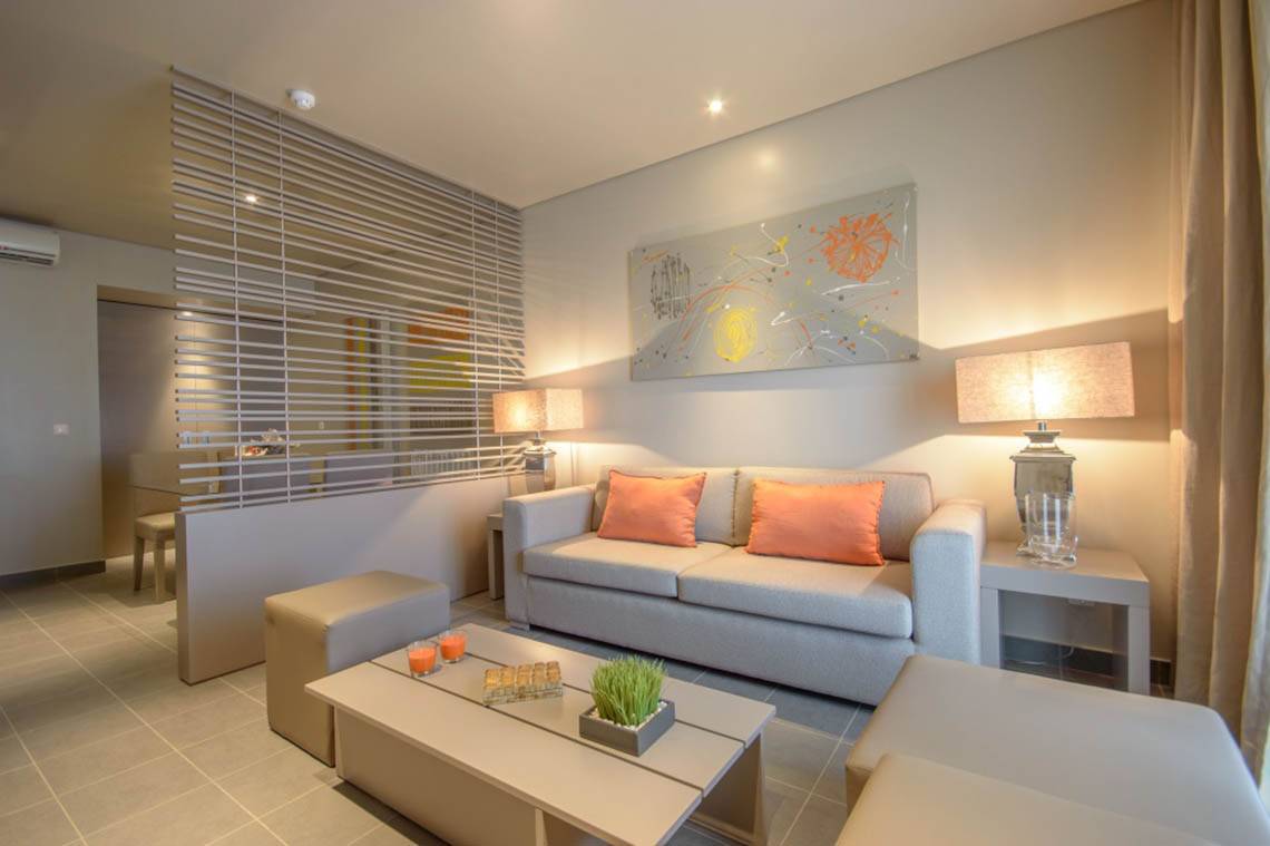 Wohnzimmer im Oasis Salinas Sea Hotel mit grauer Couch, orangen Kissen und modernen Kunstwerken.
