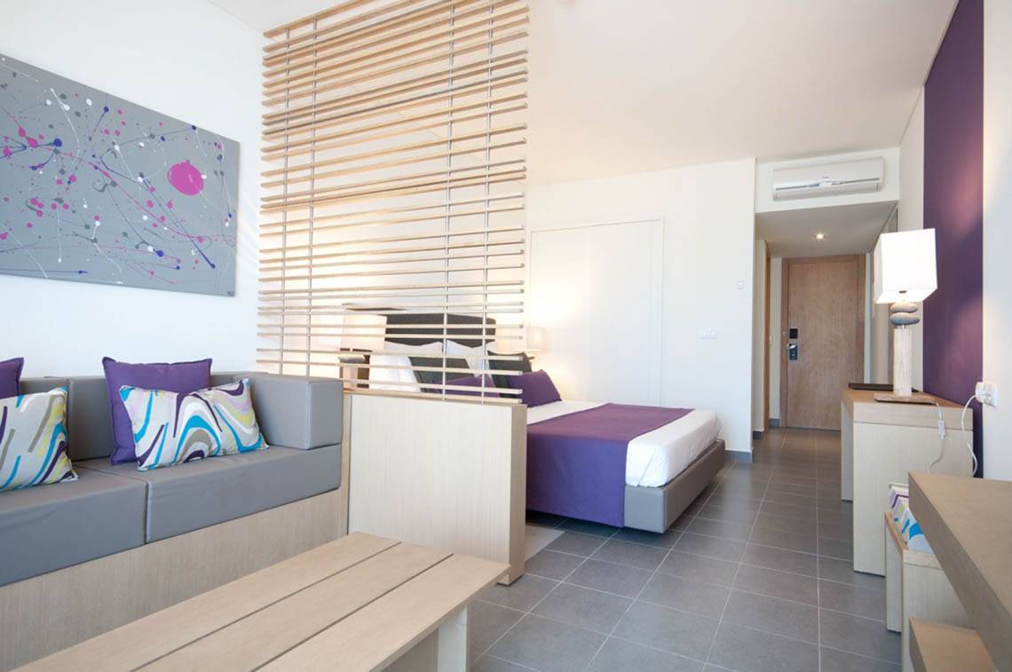 Innenansicht eines Hotelzimmers im Oasis Salinas Sea Hotel mit Bett, Sofa und moderner Einrichtung.