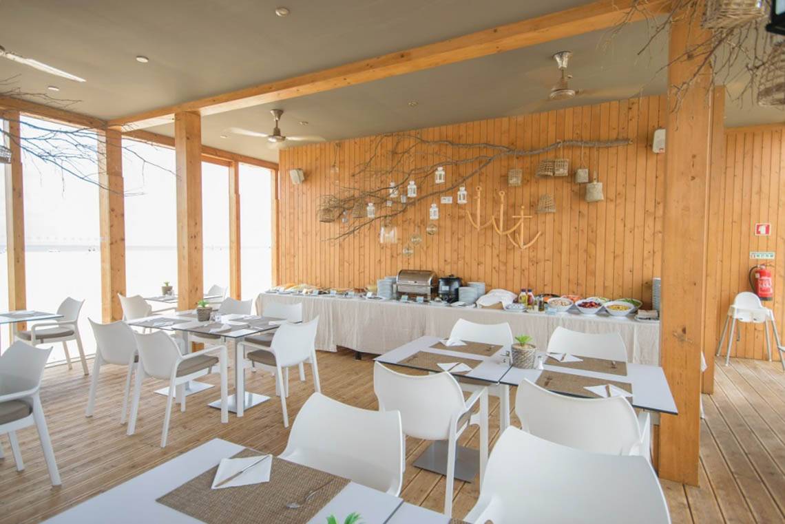 Innenansicht des Restaurants im Oasis Salinas Sea Hotel mit weißen Tischen und Stühlen und hölzernen Wänden.